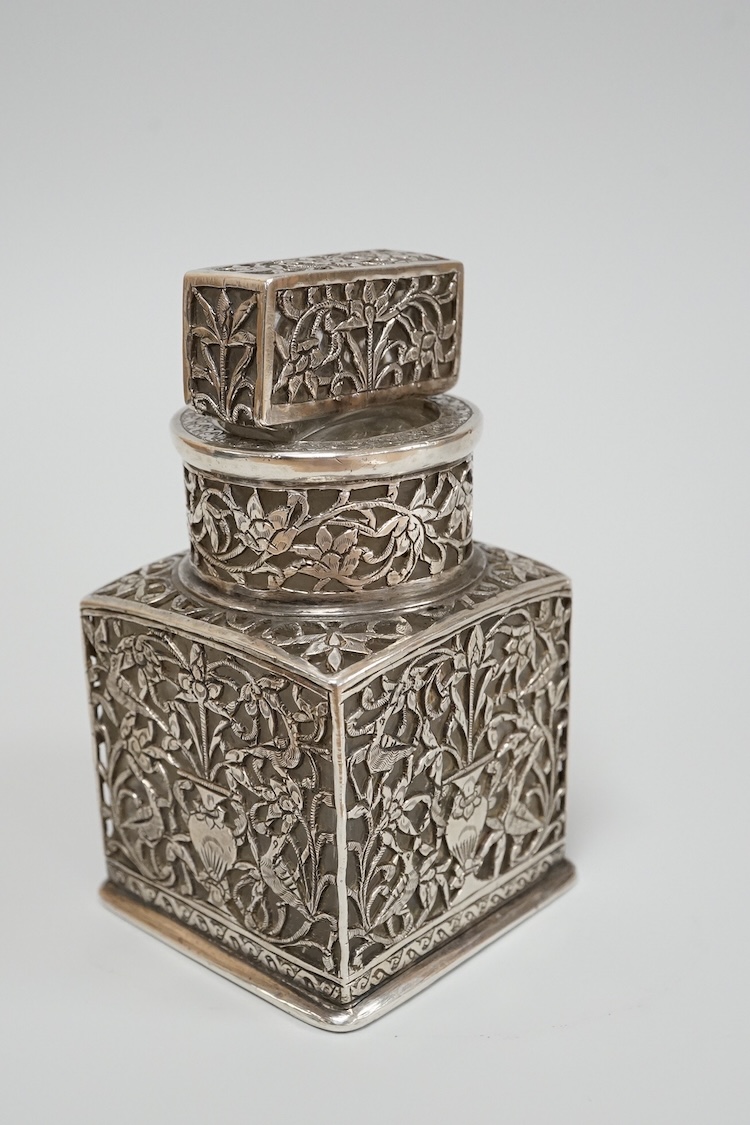 A Persian pierced white metal overlaid moulded glass salts bottle with stopper, decorated with urns and birds amid scrolling foliage, overall height 94mm.
